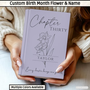 May include: A light purple hardback book featuring a black line art illustration of a daffodil flower. The text reads Chapter THIRTY, the name TAYLOR, and the phrase Every chapter brings new growth in a mix of script and serif fonts.