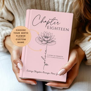 Pode incluir: Um livro rosa com o título "Chapter Eighteen" e uma ilustração floral. O livro também inclui o texto "A Story of Strength July Flower-Water Lily" e "Every Chapter Brings New Gr". O livro é segurado com as duas mãos.