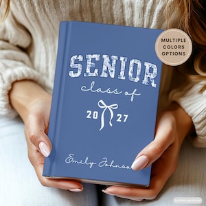 Puede incluir: Un diario de tapa dura azul con el texto SENIOR en un patrón floral blanco, seguido del texto en cursiva class of, un gráfico de lazo blanco, los números 20 27 y el nombre Emily Johnson. Una insignia circular dice MULTIPLE COLORS OPTIONS.