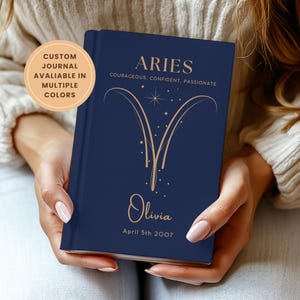 May include: A dark blue journal featuring gold text and an Aries zodiac symbol. The cover is personalised with the name "Olivia" and the date "April 5th 2007". The text "CUSTOM JOURNAL AVALIABLE IN MULTIPLE COLORS" is also visible.