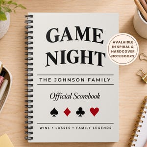 May include: A spiral-bound notebook with a white cover featuring the black text GAME NIGHT, THE JOHNSON FAMILY, and Official Scorebook. Below the text are black and red playing card suit symbols, followed by WINS, LOSSES, FAMILY LEGENDS.