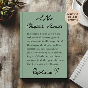 May include: A sage green hardcover book with black text that reads A New Chapter Awaits, followed by an inspirational paragraph and the name Stephanie with a heart symbol. A circular badge in the top right corner states Multiple Colors Options.