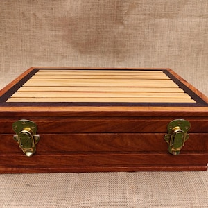 May include: A rectangular wooden box with a light brown, slatted top and dark brown trim. The box is made of dark brown wood with brass-colored clasps. The box is closed and sits on a neutral-colored surface.