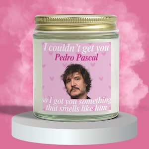 Può includere: Un barattolo di candela bianco con un'etichetta rosa che mostra una foto di Pedro Pascal e il testo "Non ho potuto prenderti Pedro Pascal, quindi ti ho preso qualcosa che profuma come lui."