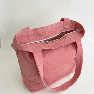 May include: A pink tote bag with a zip closure. The bag has two handles and is made of a robust fabric. The zip is silver, and the interior lining is visible.