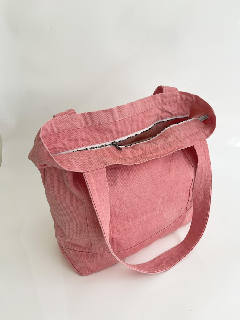 May include: A pink tote bag with a zip closure. The bag has two handles and is made of a robust fabric. The zip is silver, and the interior lining is visible.