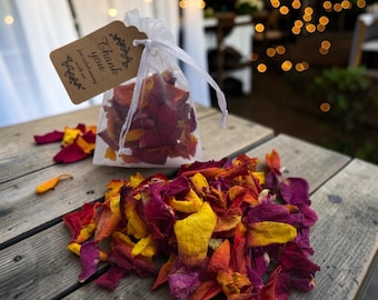 May include: A sheer white drawstring pouch filled with dried flower petals in shades of deep magenta, orange, and yellow. A brown rectangular paper tag is attached to the drawstring, featuring the printed text, Thank you for celebrating with me.