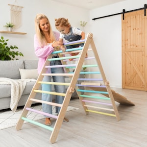 Può includere: Un triangolo da arrampicata in legno con pioli dai colori pastello, tra cui rosa, blu, giallo e viola. La struttura presenta un telaio triangolare con una rampa in legno collegata alla base, progettata per l'attività fisica al chiuso.