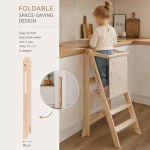 Può includere: Una torre di apprendimento in legno chiaro con design pieghevole. Il testo recita FOLDABLE SPACE-SAVING DESIGN, Easy to fold and store when not in use. Only 10 cm in depth! La struttura presenta un pannello posteriore in tessuto beige e due gradini.
