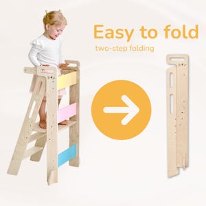Può includere: Uno sgabello in legno con un design colorato, con un bambino in piedi sul gradino superiore. Lo sgabello si piega per facilitarne la conservazione, con una freccia che punta allo sgabello piegato sul lato destro dell'immagine. Il testo "Easy to fold" e "two-step folding" è visualizzato sopra la freccia.