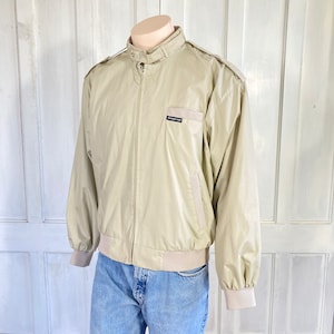 May include: A beige bomber jacket with a zipper closure and a brown logo patch that reads "Members Only" on the left chest.