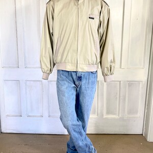 May include: A beige bomber jacket with a zipper closure and a small logo on the left chest. The jacket has a ribbed collar, cuffs, and waistband.