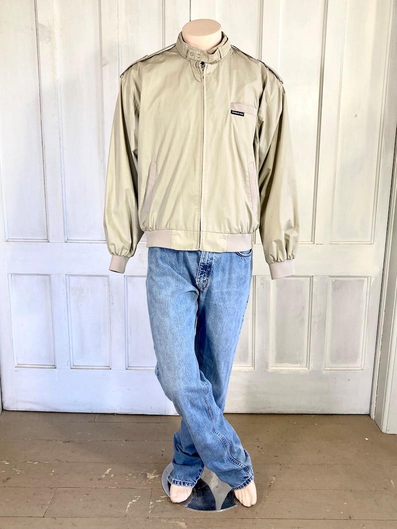May include: A beige bomber jacket with a zipper closure and a small logo on the left chest. The jacket has a ribbed collar, cuffs, and waistband.