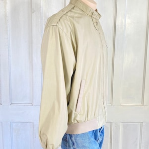 May include: A beige lightweight jacket with a zipper closure and a stand-up collar. The jacket has a single pocket on the left side and a ribbed waistband.