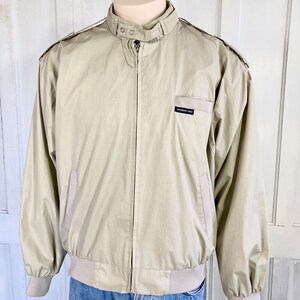 May include: A beige Members Only jacket with a zipper closure and a ribbed waistband. The jacket has a stand-up collar and two pockets on the front.