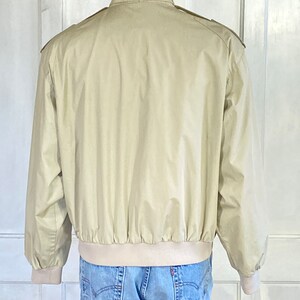 May include: A beige bomber jacket with a stand-up collar and a ribbed waistband.