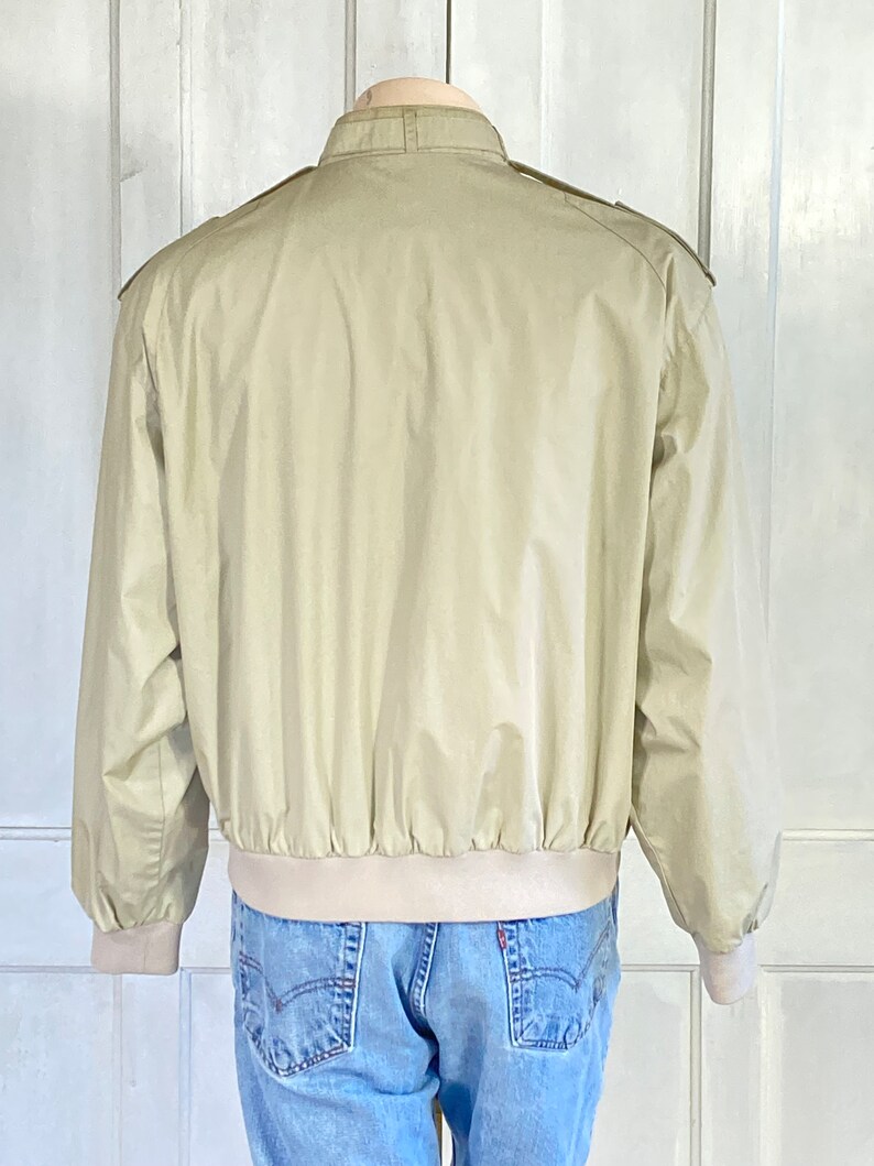 May include: A beige bomber jacket with a stand-up collar and a ribbed waistband.