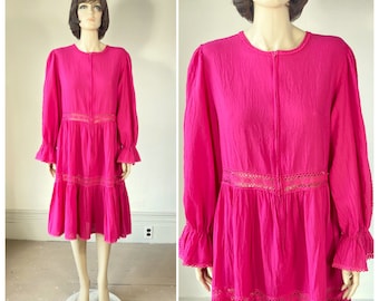 Könnte beinhalten: Ein leuchtend fuchsiafarbenes knielanges Kleid mit langen Ärmeln mit gerüschten Bündchen, einem Rundhalsausschnitt und einer Knopfleiste vorne. Das Kleidungsstück ist mit horizontalen Bändern aus filigraner Lochspitze an Taille und Rock verziert.