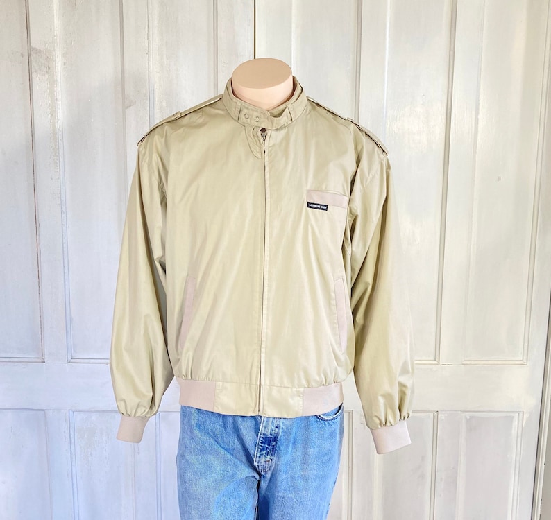 May include: A beige bomber jacket with a zipper closure and a black logo that reads "Members Only" on the left chest.
