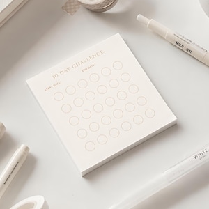 May include: A square off-white notepad featuring the text 30 DAY CHALLENGE, START DATE, and END DATE in a light font. The notepad includes a grid of thirty empty circles arranged in five rows and six columns for tracking daily progress.