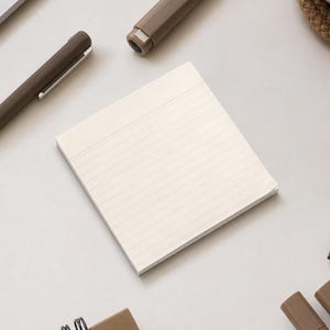 May include: A square notepad with cream-colored paper featuring thin horizontal lines. The notepad is surrounded by various stationery items including brown pens, a brown binder clip, and a small portion of a spiral-bound notebook.