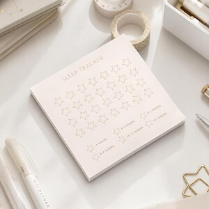 May include: A square notepad with a light cream background featuring the text SLEEP TRACKER at the top. The page contains a grid of outlined stars for tracking sleep, with additional star icons labeled with hour ranges from <4 hours to 12+ hours.