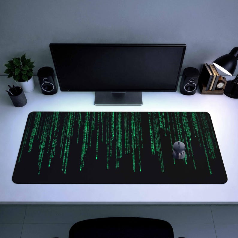 Puede incluir: Alfombrilla de escritorio rectangular negra con un patr&oacute;n de lluvia digital verde, un rat&oacute;n de ordenador y un monitor de ordenador. La alfombrilla mide aproximadamente 91 cm de largo y 30 cm de ancho. La configuraci&oacute;n incluye altavoces, una l&aacute;mpara de escritorio y una peque&ntilde;a planta en maceta.