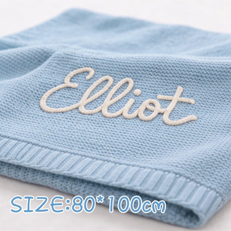 May include: A light blue knitted blanket with the name "Elliot" embroidered in cream-colored thread. The blanket measures 31.5 x 39.4 inches. The blanket has a ribbed border.