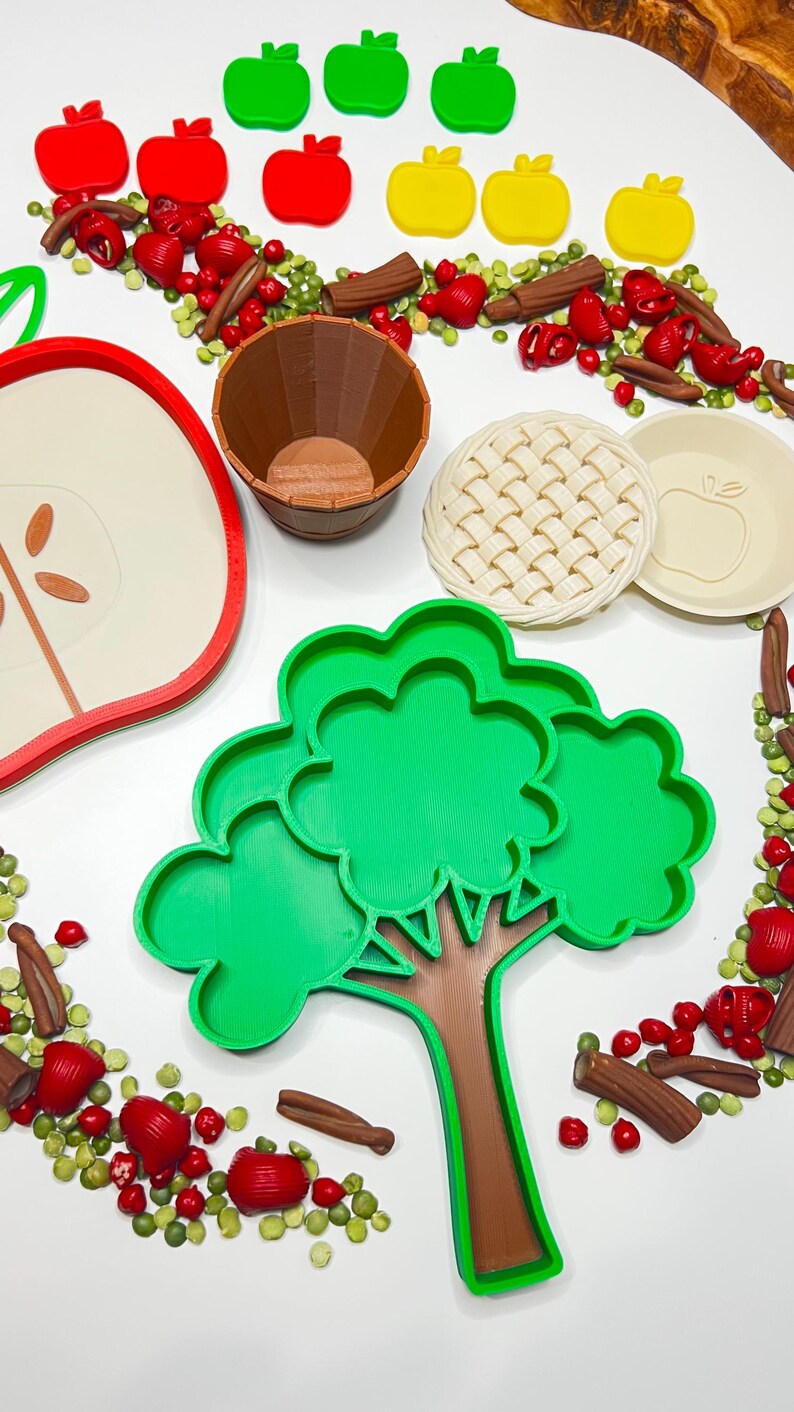 May include: A collection of colorful, food-themed cookie cutters and decorative elements. Includes red, green, and yellow apple shapes, a tree, a pie crust, a pie plate, a wooden barrel, and decorative elements.