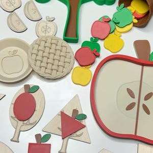 May include: A collection of wooden and colorful apple-themed educational toys. Includes apple slices, a pie crust, a tree, and various apple shapes in red, green, and yellow. The toys are designed for learning and play.