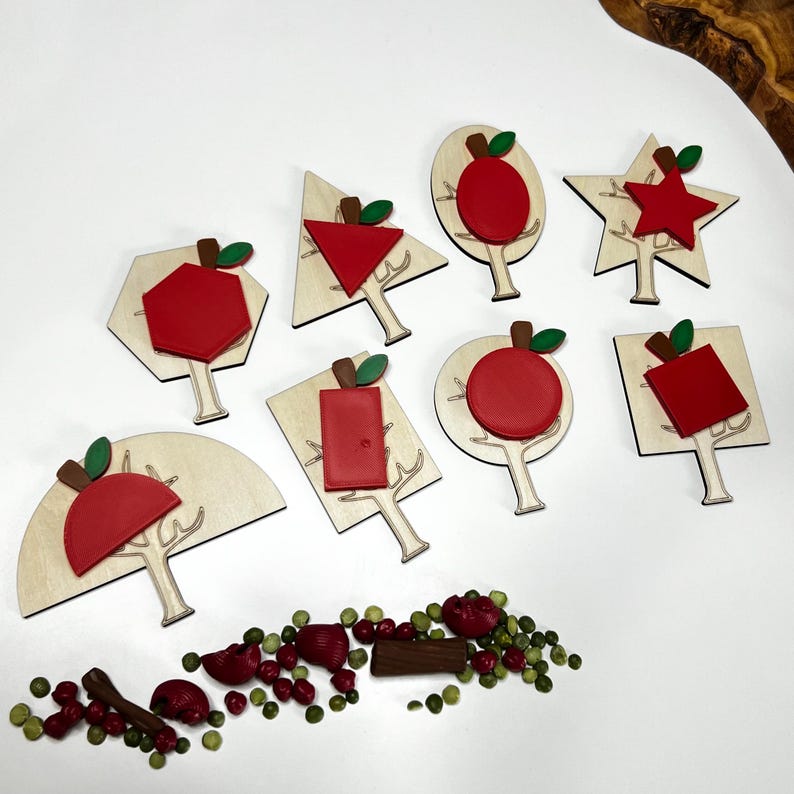 May include: Wooden puzzles featuring red apple shapes in various geometric forms, including a hexagon, triangle, and star. Each puzzle piece has a brown stem and green leaf. A collection of red and green decorative items are scattered below.
