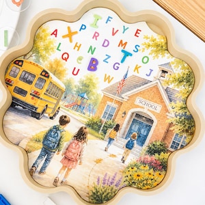 May include: A flower-shaped wooden tray containing a school-themed illustration with a yellow bus, children with backpacks, and a brick building labelled SCHOOL. The tray surface features scattered colourful plastic alphabet letters including A, B, and T.