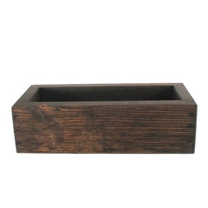 May include: A dark brown wooden rectangular box with a slightly raised lip around the top edge. The box is made of natural wood with a rustic finish.