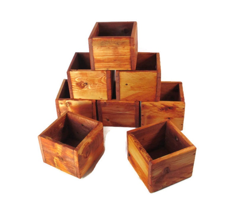 May include: A set of eight wooden boxes stacked in a pyramid shape. The boxes are made of natural wood with a reddish-brown stain. The boxes are all the same size and shape, and they have a rustic look.