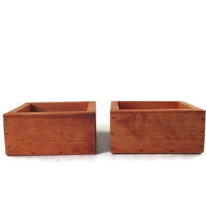 May include: Two wooden square boxes with a reddish-brown stain. The boxes are empty and have a rustic look.