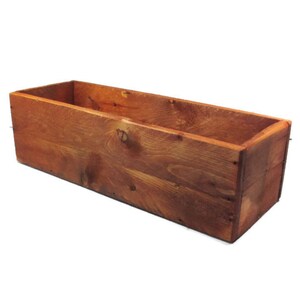 May include: A rectangular wooden planter box with a natural wood stain finish. The planter is empty and ready for planting.