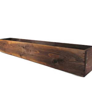 Puede incluir: Una jardinera de madera rectangular y larga, con una mancha de color marr&oacute;n oscuro. La jardinera est&aacute; hecha de madera natural con grano y nudos visibles.