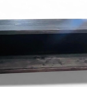 May include: A rectangular, dark-stained wooden shelf with an open front. The shelf is a long, narrow box shape, with visible wood grain. The interior is dark, creating a contrast with the lighter edges. The shelf is designed for wall mounting.