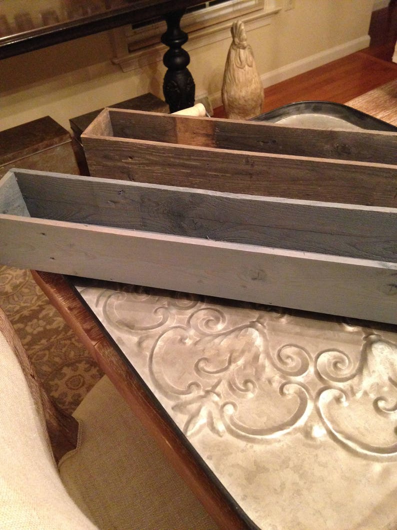 Puede incluir: Dos jardineras de madera, una gris y otra marr&oacute;n, est&aacute;n apiladas una encima de la otra. Las jardineras est&aacute;n hechas de madera reciclada y tienen un aspecto r&uacute;stico. Las jardineras est&aacute;n sobre una mesa con una superficie de metal decorativa.