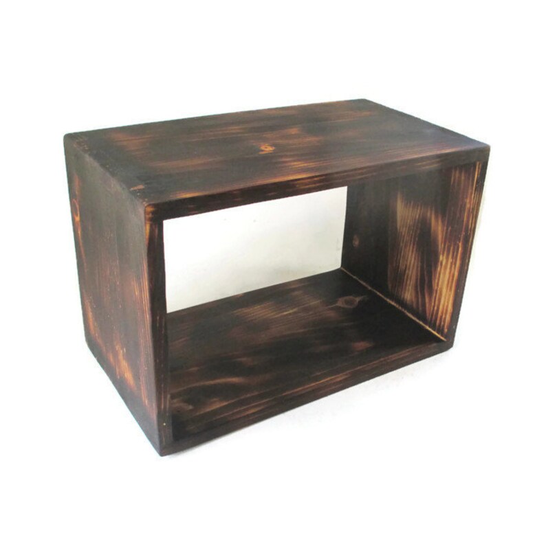 May include: A dark brown wooden shelf unit with a single open shelf. The shelf is made of unfinished wood with a rustic, distressed look.