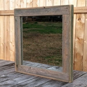 May include: A square mirror featuring a wide, flat frame constructed from weathered, gray-toned reclaimed wood. The frame displays a natural, textured grain pattern with visible knots and variations in the wood surface, surrounding a clear glass.