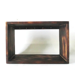 May include: A dark brown wooden frame with a rectangular opening. The frame has a distressed look and is made of unfinished wood.