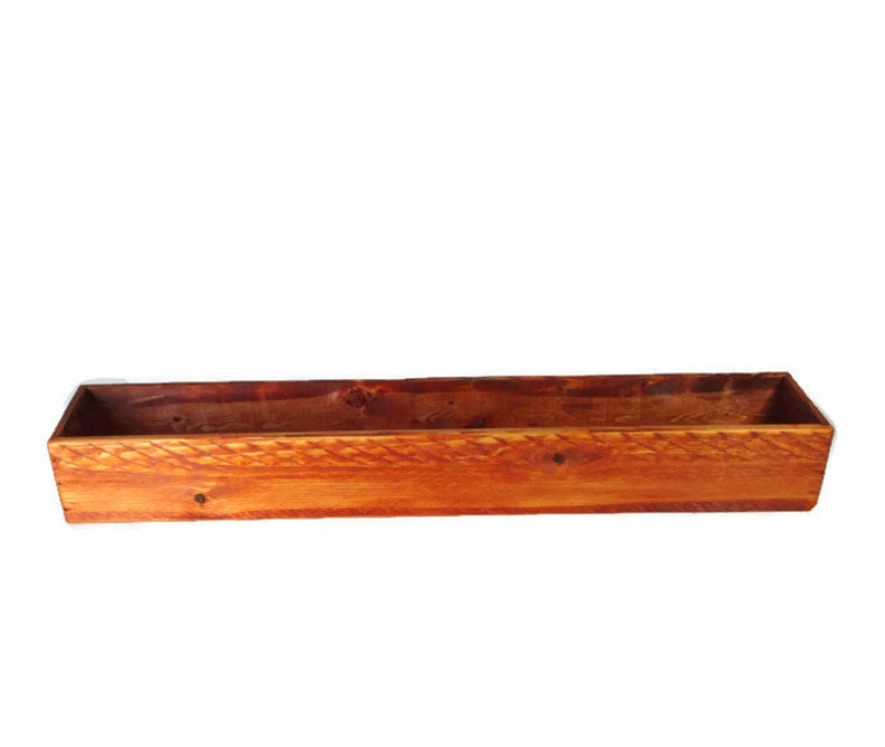 Puede incluir: Una jardinera de madera rectangular y larga, con un acabado de madera natural. La jardinera est&aacute; hecha de madera sin tratar y tiene un aspecto r&uacute;stico.
