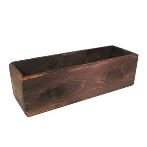 May include: A dark brown wooden planter box with a rectangular shape. The planter is made of unfinished wood and has a rustic look.
