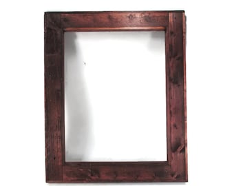 May include: A rectangular wooden frame with a dark reddish-brown stain. The frame is made of thick planks of wood, with visible wood grain and knots. The interior of the frame is empty, revealing a white background. The frame is designed for displaying artwork or photos.
