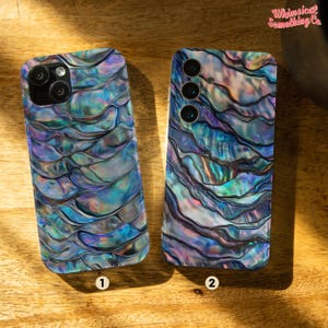 Op de afbeelding: Twee telefoonhoesjes met een blauw, groen en paars iriserend patroon dat lijkt op een schelp. De hoesjes zijn genummerd 1 en 2.