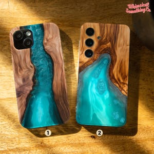May include: Two phone cases featuring a wood and blue resin design. Both cases are crafted from wood and incorporate a blue resin inlay. The resin is shaped like a river or stream. The cases are labelled with numbers 1 and 2.