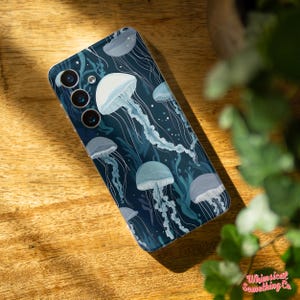 May include: A phone case with a blue background and a pattern of white jellyfish. The case has a camera cutout with three lenses.