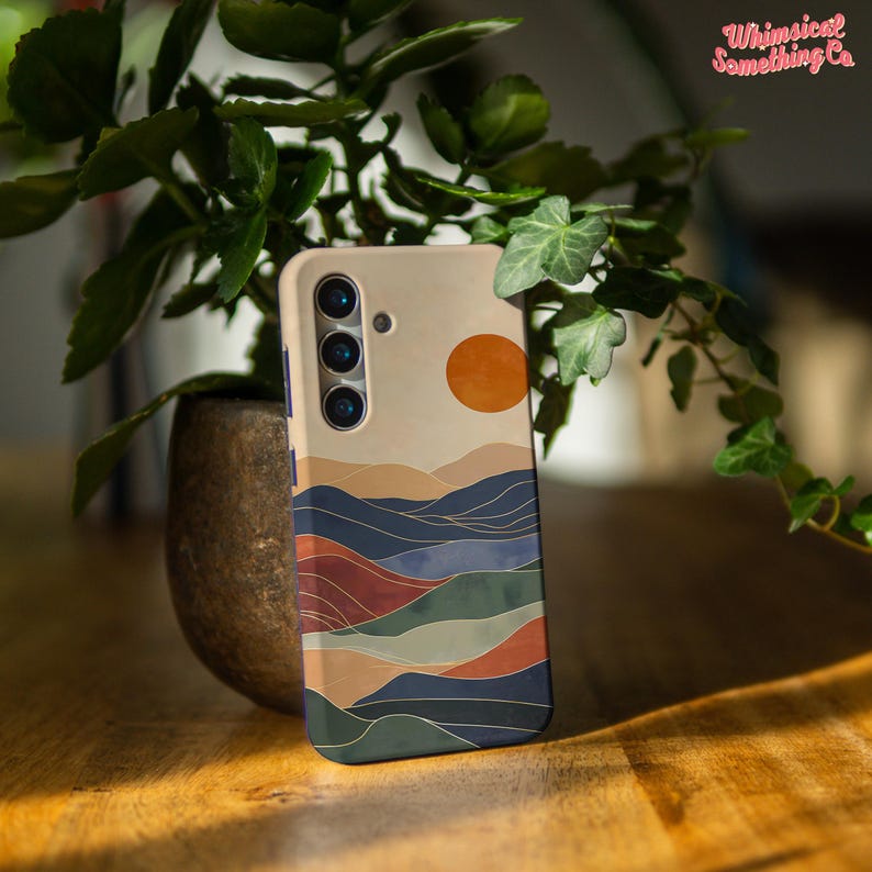 Puede incluir: Una funda para tel&eacute;fono con un dise&ntilde;o abstracto de paisaje colorido. La funda presenta una puesta de sol con un gran sol naranja, monta&ntilde;as azules y verdes, y un primer plano marr&oacute;n y naranja. La funda tiene un recorte para la c&aacute;mara con tres lentes.