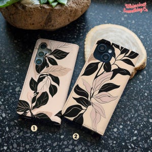May include: Two rectangular phone cases with a light beige background featuring a black and pale pink botanical leaf pattern. Each case has a camera cutout and is labeled with a small number, one or two, in a white circle at the bottom.